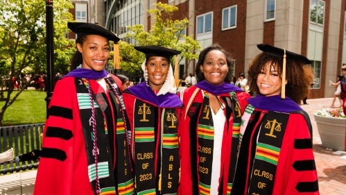 Four female students in cap and hood smiling after Commencement