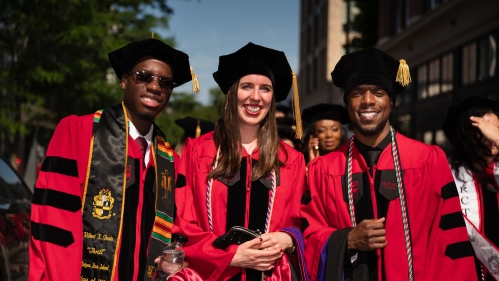 two men and one woman in red commencement robes
