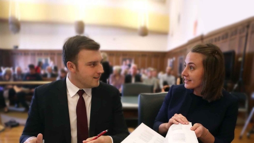Man and woman seated and talking over papers at desk