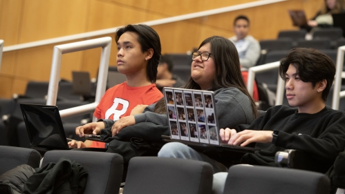 Three students seated in a row pay attention to a lecture.