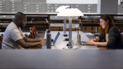 Man and woman on laptops working across from each other in library