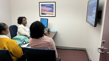 Three students at desk looking at monitor