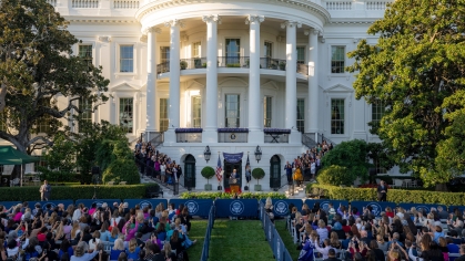 wide shot of the White House with people seated on the lawn