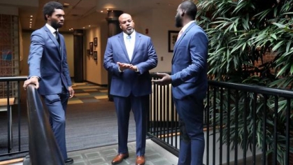 three men in suits standing and conversing with one another