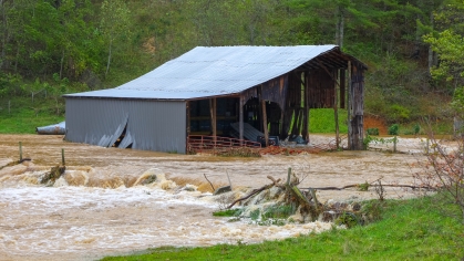 destroyed barn sitting amid brown flood waters