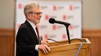 Man in suit and glasses smiling at a podium looking at audience