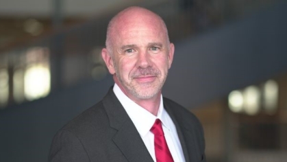 man in black suit and red tie looking ahead