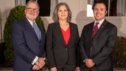Two men and one woman smiling in dark suits