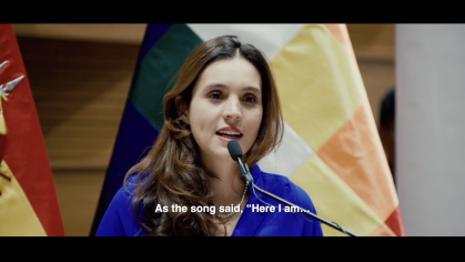 woman speaking at mic with flags behind her