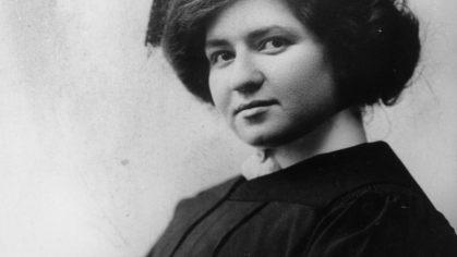 black and white image of woman sitting in black graduation cap and gown