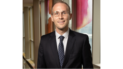 man in dark suit wearing glasses and smiling in front of painted windows