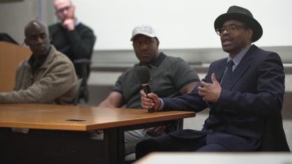 Group of three men seat at table with another at podium in the back
