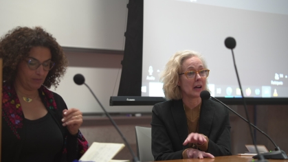 two women at table in front of classroom with mics