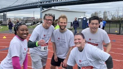 group of people in matching shirts smiling on race track with bridge in background