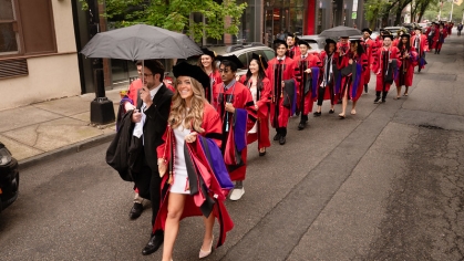 Line of graduates in red gowns walking in the street