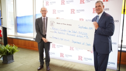 two men holding giant check in front of Rutgers Law step and repeat
