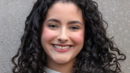 woman with long curly hair smiling in front of gray background