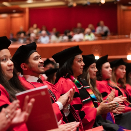 people seated next to each other in red graduation robes and black caps