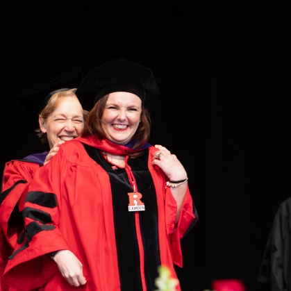 woman in red robe and black cap being hooded on stage