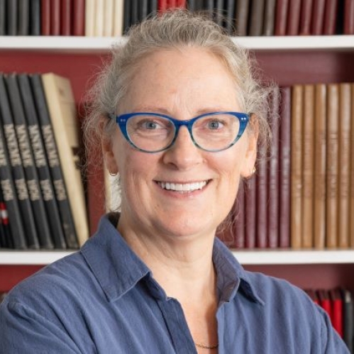 woman in blue glasses smiling in front of bookcase