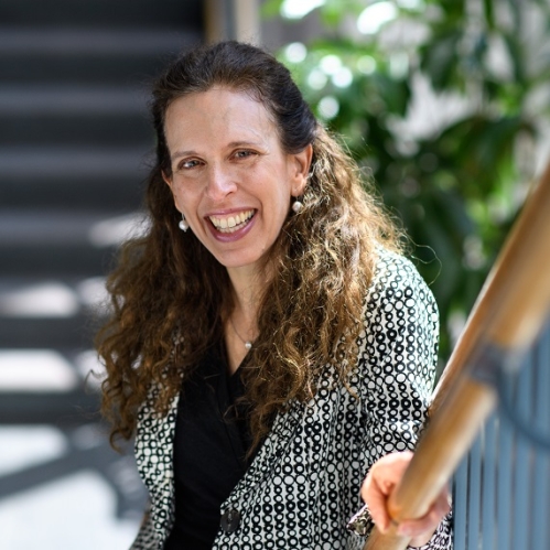 Woman smiling with teeth wearing black shirt and black and white patterned jacket