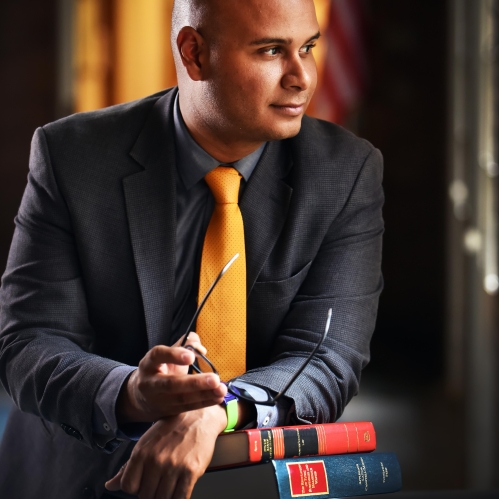Man looking to the side with his arms on a stack of textbooks holding glasses