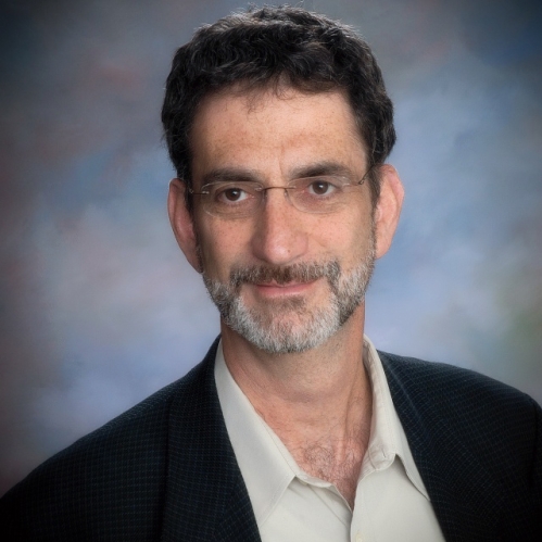 Man grinning wearing glasses and a suit with white shirt.