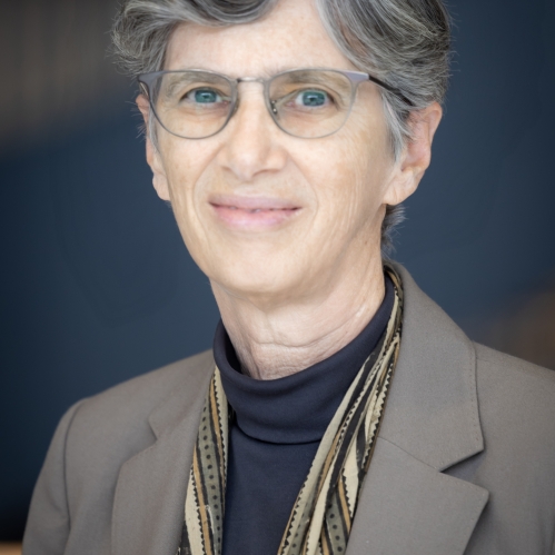 Woman grinning wearing glasses, turtleneck, suit jacket, and scarf