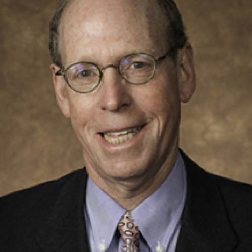 Man smiling wearing glasses, blue button down shirt, tie, and suit jacket