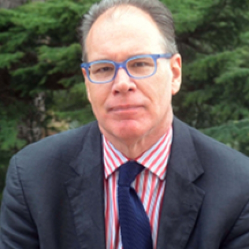 Man grinning wearing glasses, a pink and white striped shirt, blue tie, and suit jacket