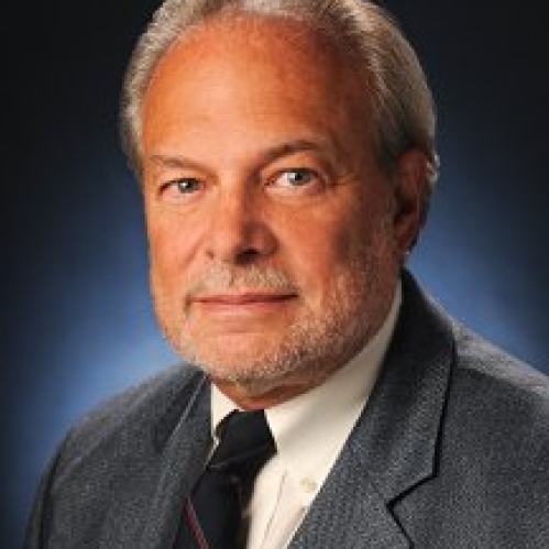 Man lightly grinning wearing white button down and grey suit jacket with black tie