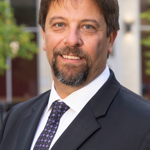 Man grinning wearing white button down shirt, blue tie, and suit jacket
