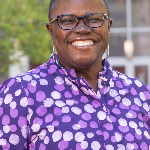 Woman smiling with glasses wearing a purple shirt