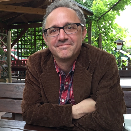 Man grinning wearing glasses and multicolored shirt