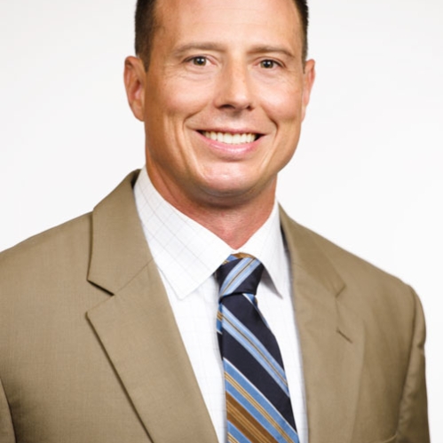 Man smiling wearing white button down, striped tie, and tan suit