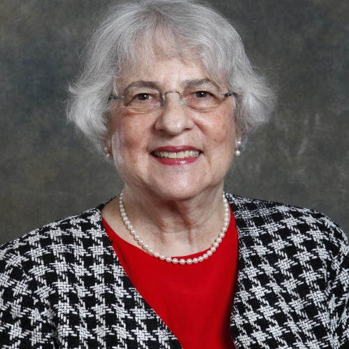 Woman smiling with glasses, red shirt, and black and white houndstooth jacket
