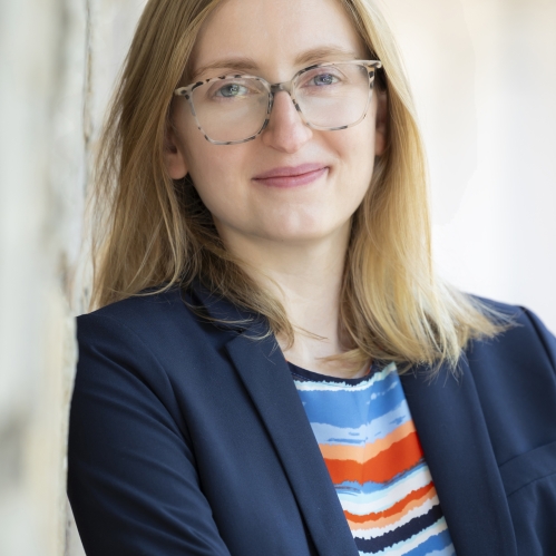 Woman grinning with glasses, multi-colored shirt, and suit jacket