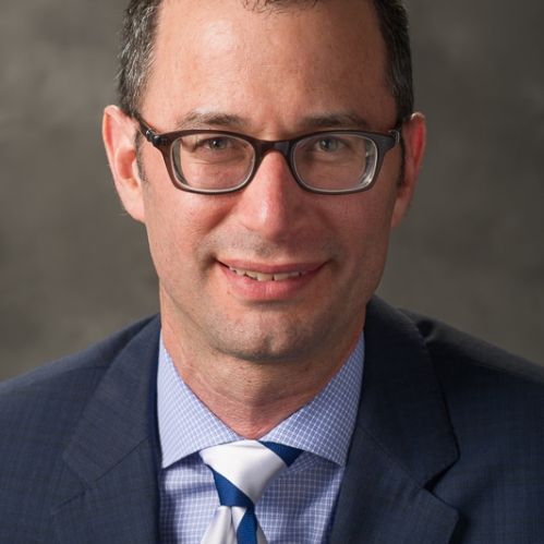 Man grinning who is wearing glasses and a blue tie