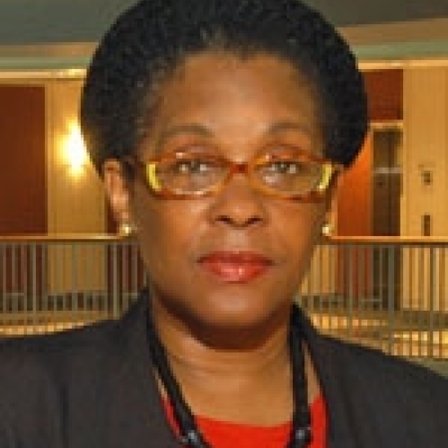 Woman grinning with glasses, wearing a red shirt and black suit jacket