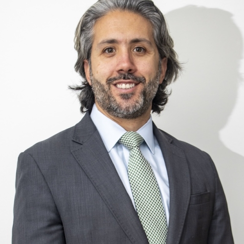 Man in grey suit and green tie smiling in front of white wall