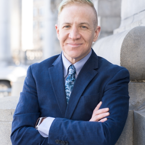 Man in blue suit smiling and leaning on building facade outdoors