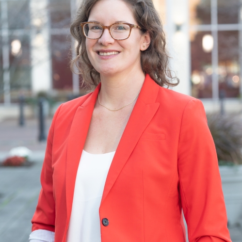 woman smiling outdoors in bright red/orange blazer and wearing glasses