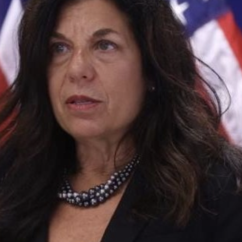 Woman grinning in front of an American flag wearing a black blazer.
