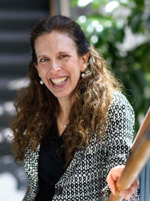 Woman smiling with teeth wearing black shirt and black and white patterned jacket