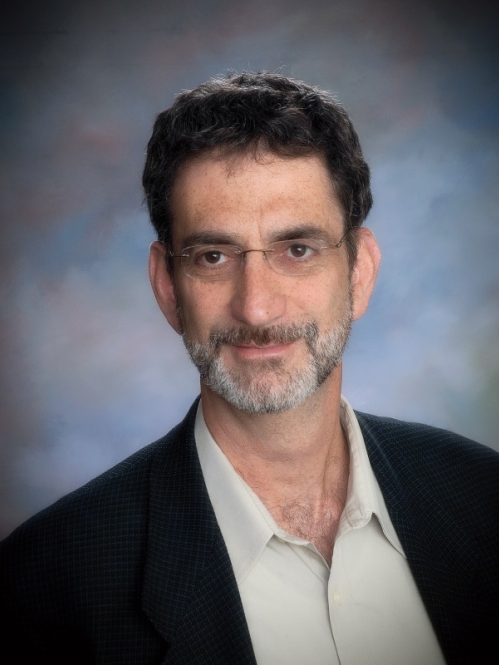 Man grinning wearing glasses and a suit with white shirt. 