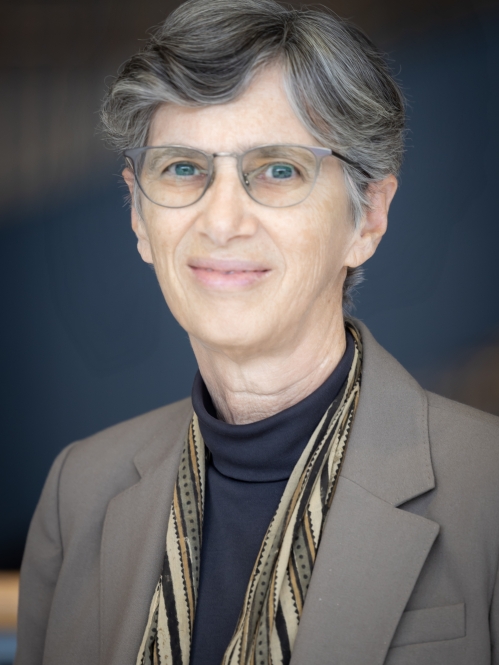 Woman grinning wearing glasses, turtleneck, suit jacket, and scarf