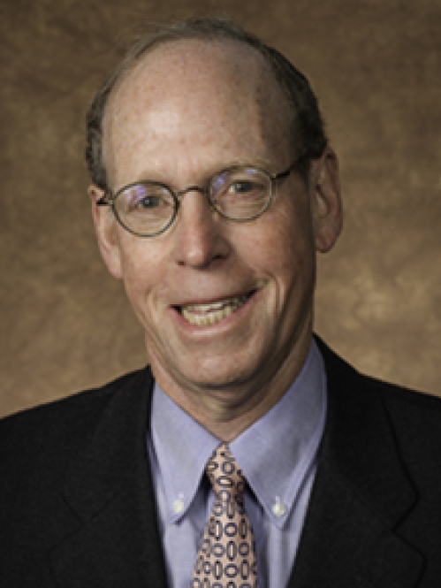 Man smiling wearing glasses, blue button down shirt, tie, and suit jacket