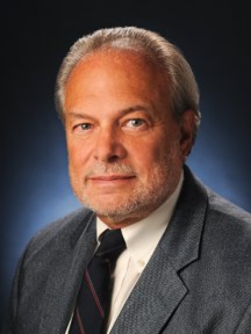 Man lightly grinning wearing white button down and grey suit jacket with black tie 