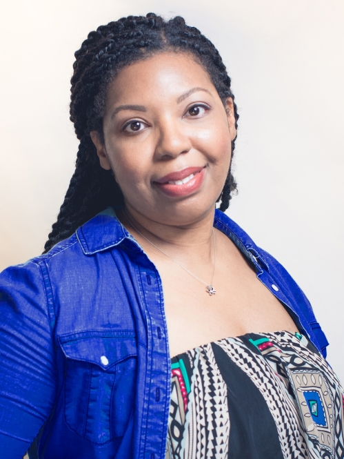 Woman grinning wearing multi-colored shirt and blue jacket