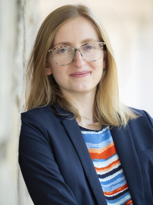 Woman grinning with glasses, multi-colored shirt, and suit jacket